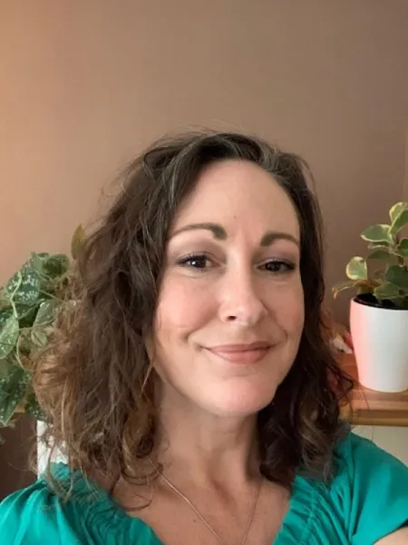 Brunette woman smiling at the camera wearing a green shirt.